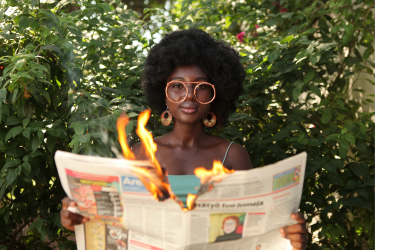 woman with afro and glasses holding a burning newspaper