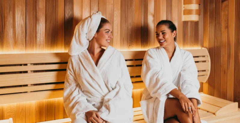 2 women in robes sitting in a sauna